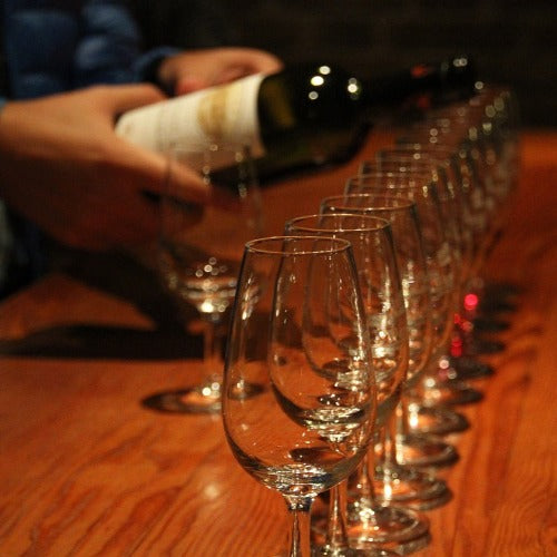 tasting glasses and a person holding a bottle of wine ready to pour.